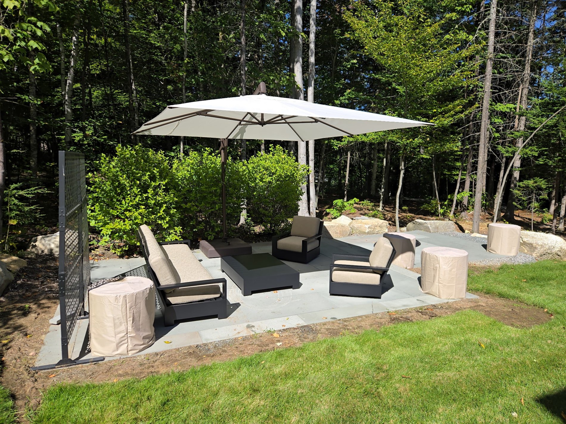 Fernwood patio with outdoor seating and umbrella beside woodland