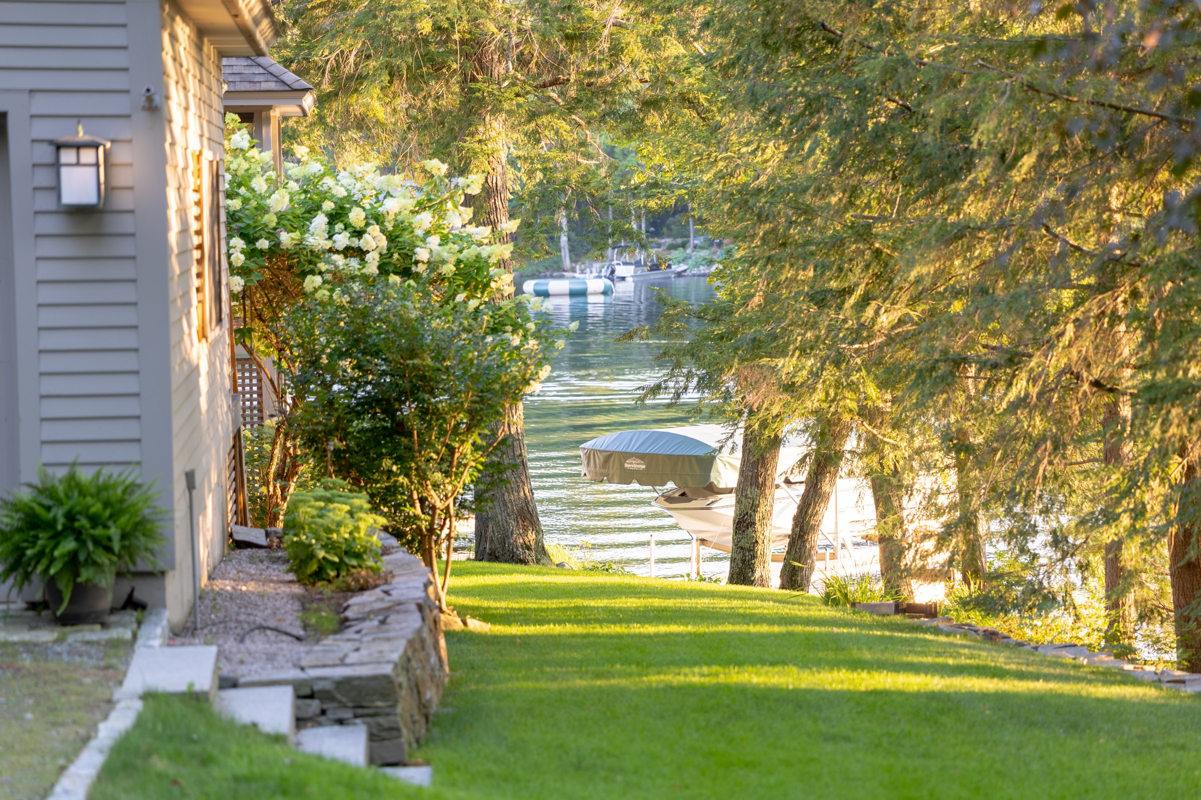 Sunlit lawn leading past Woodland through trees toward the waterfront